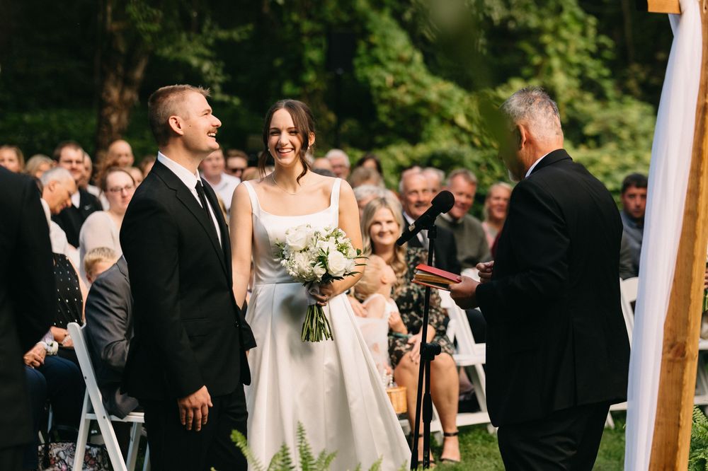 Wedding guests gather outdoors under trees during a summer ceremony celebration.