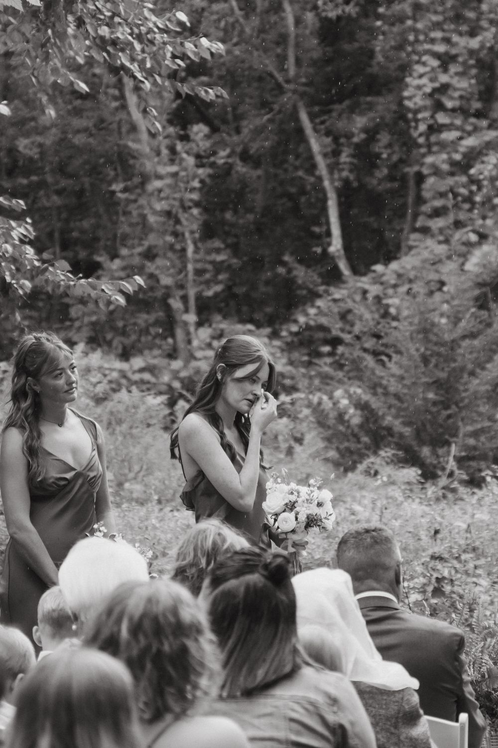 Wedding guests watching an emotional outdoor ceremony while seated in white chairs surrounded by greenery.