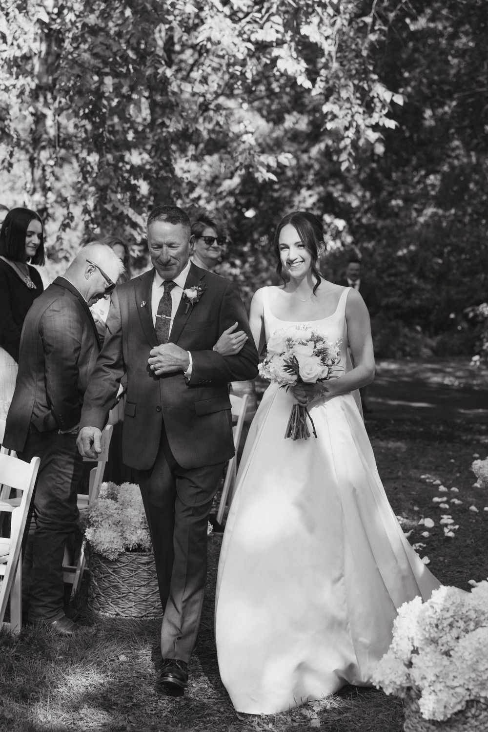 Black and white wedding ceremony photos show couple walking down aisle together surrounded by guests outdoors.