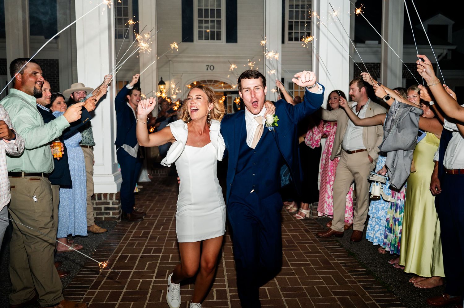 Wedding couple exits venue through sparkler tunnel lined with guests.