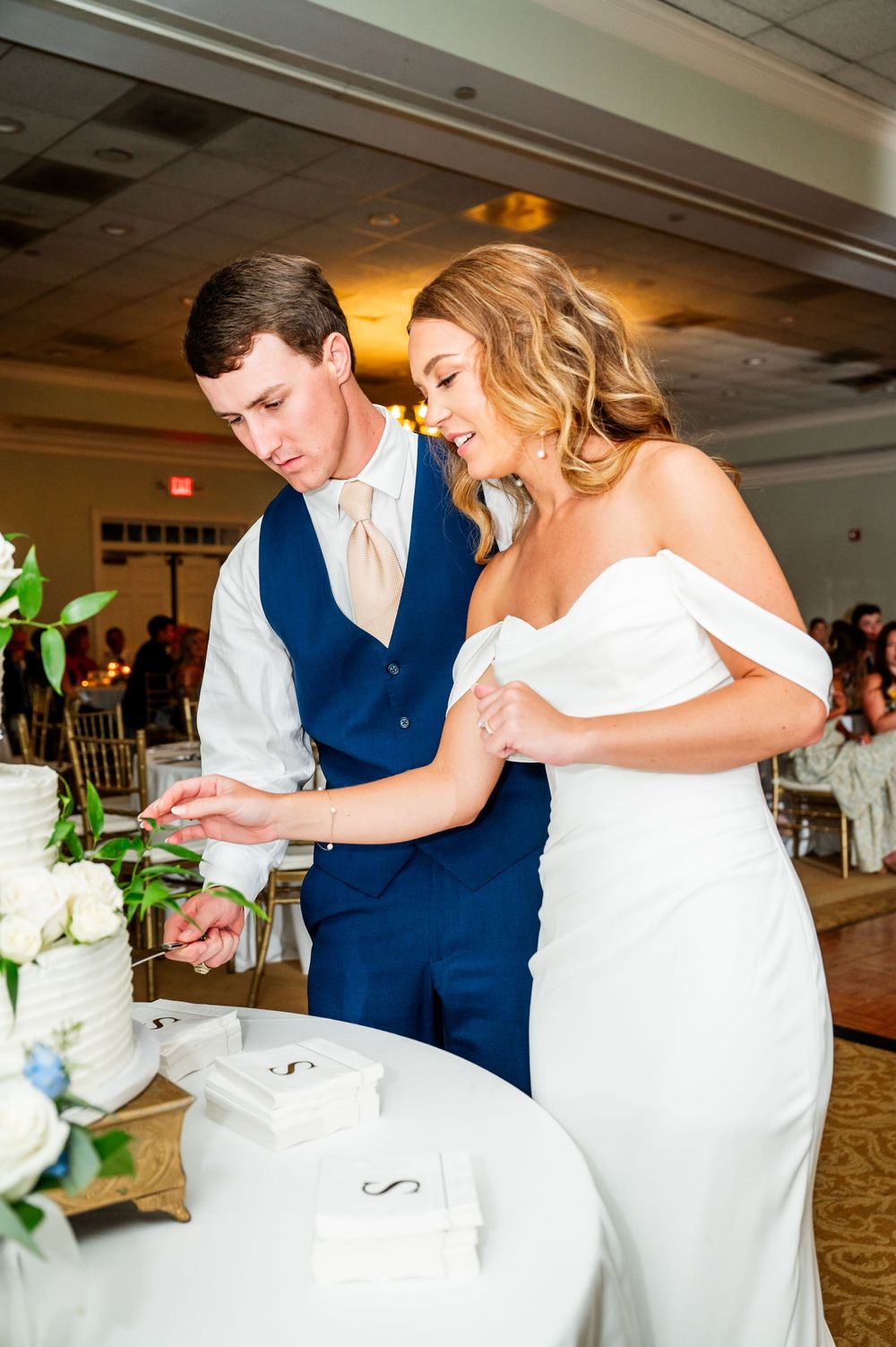 Newlyweds sharing cake at their wedding reception in an elegant ballroom.