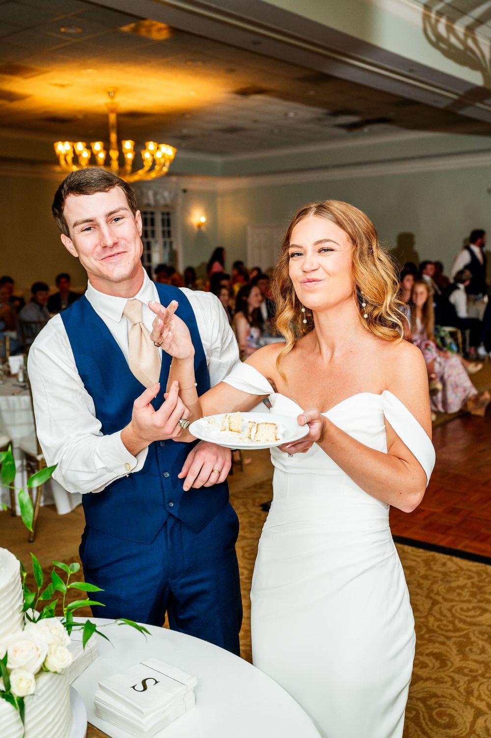 Wedding couple playfully feeding each other cake during reception celebration.