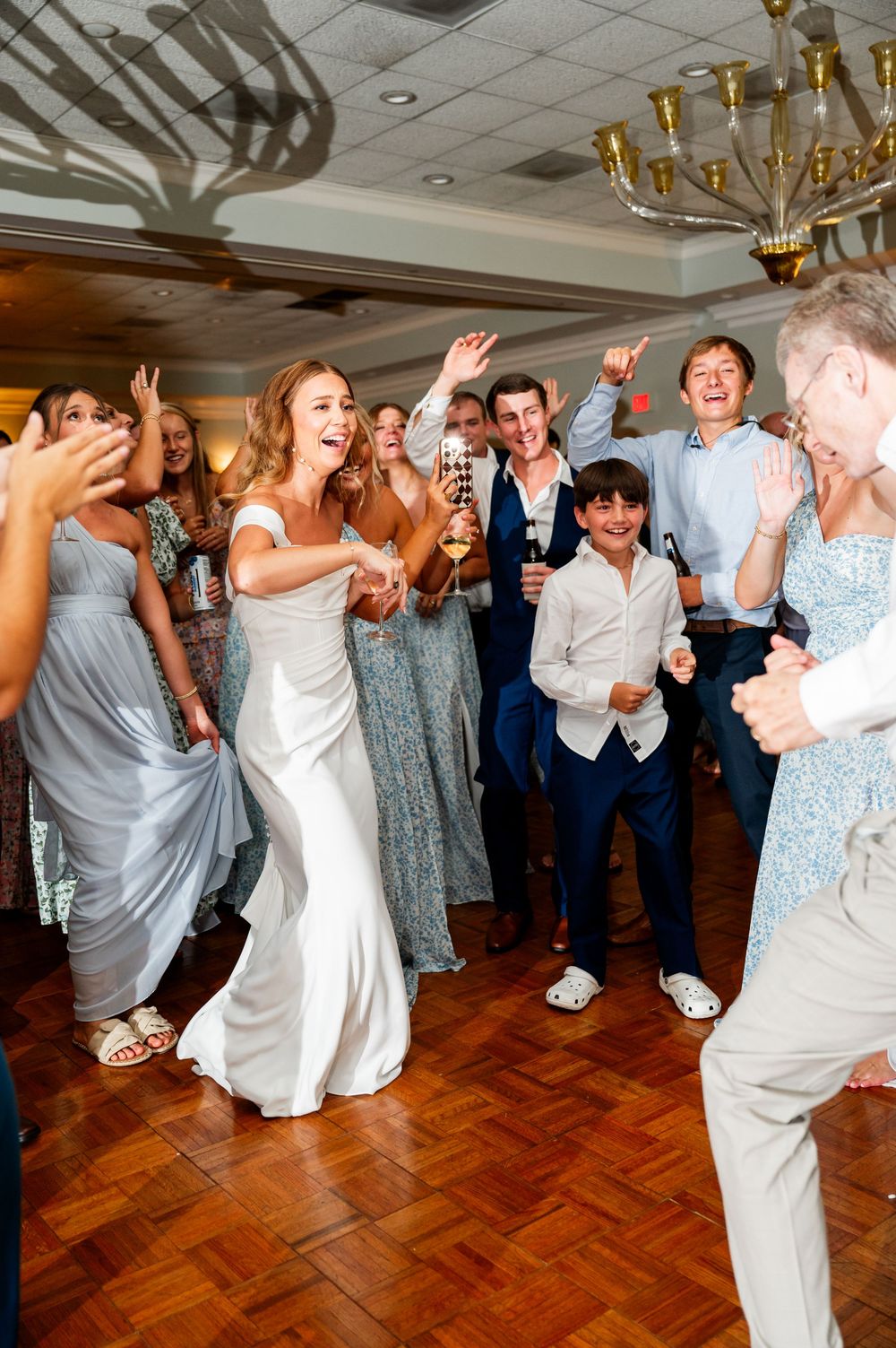 Wedding guests dancing and celebrating on wooden dance floor at reception.