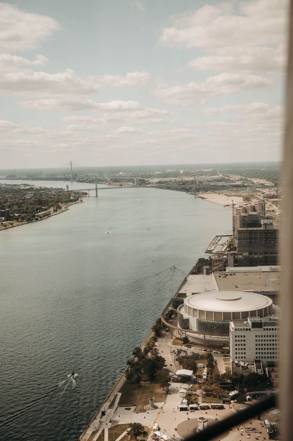 Aerial view of Detroit riverfront with Ambassador Bridge and city skyline on cloudy day.