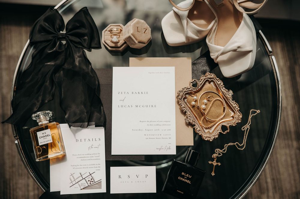 Elegant wedding flat lay with Chanel perfume, invitation suite, heels, and gold jewelry.