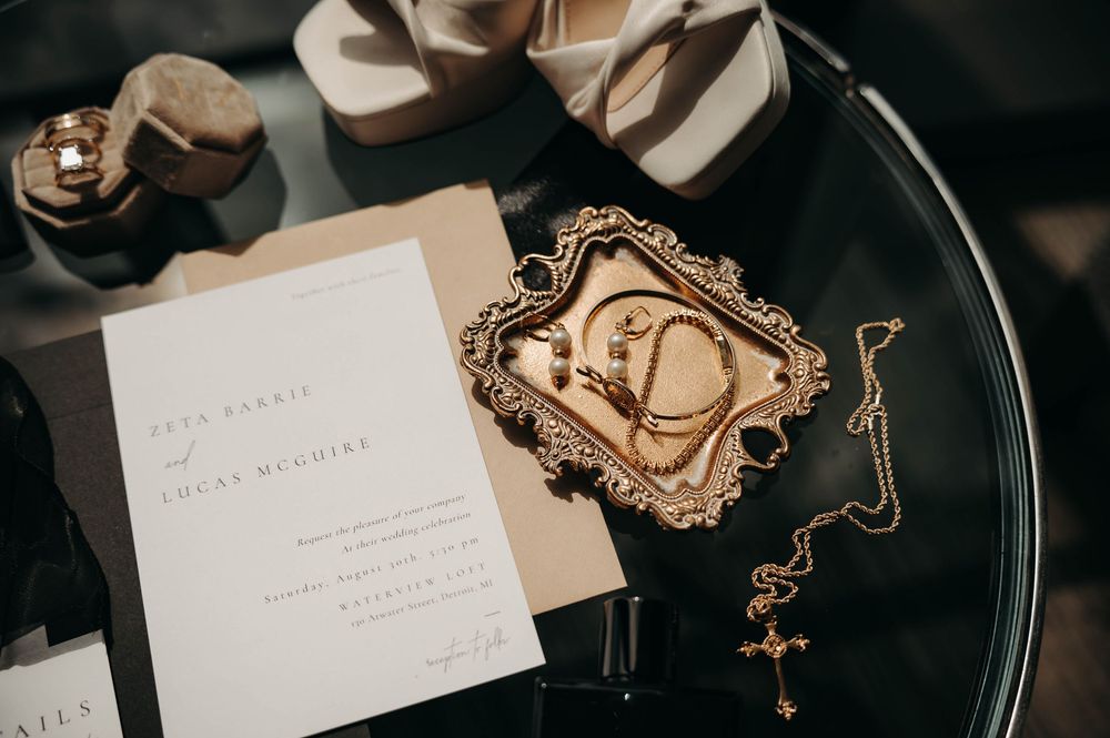 Close-up of wedding invitation suite with gold jewelry tray and bridal accessories on glass table.