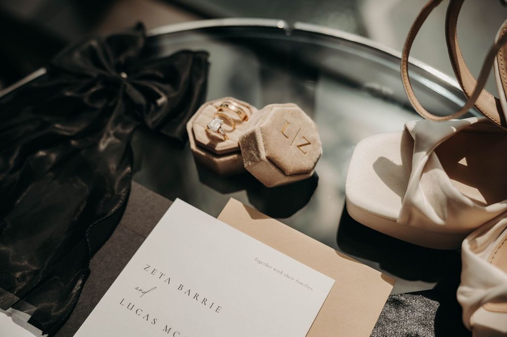 Hexagonal velvet ring box with wedding bands beside bridal heels and wedding invitation.