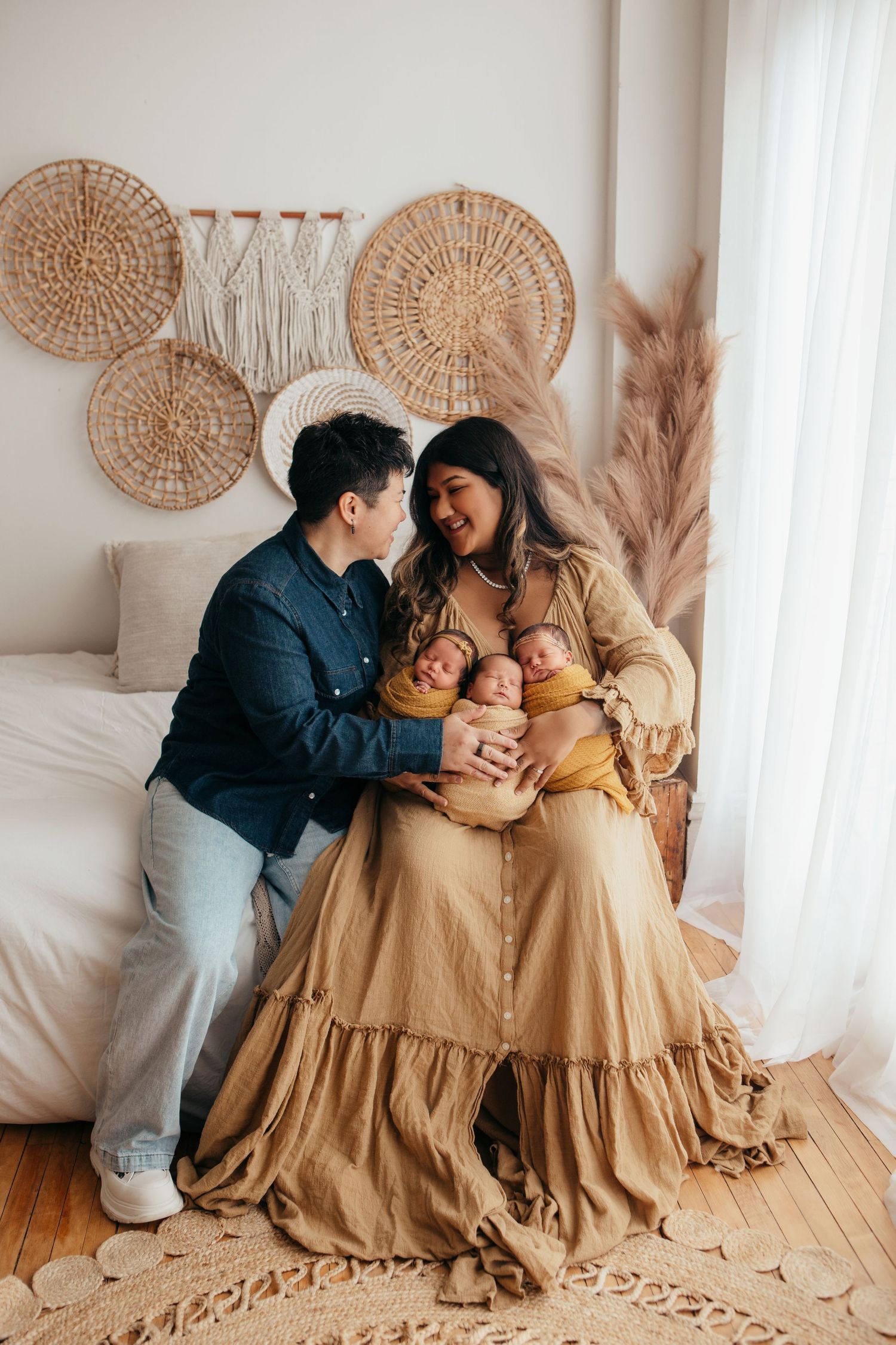 A heartwarming family photo session featuring matching tan dresses against a neutral backdrop with woven wall decor.