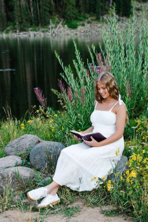 female sitting next to body of water reading bible