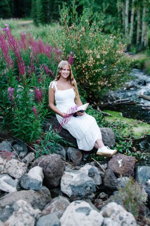 female sitting next to creek reading bible