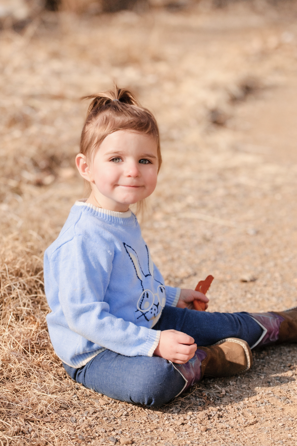child sitting on dirt path holding carrots in hand content