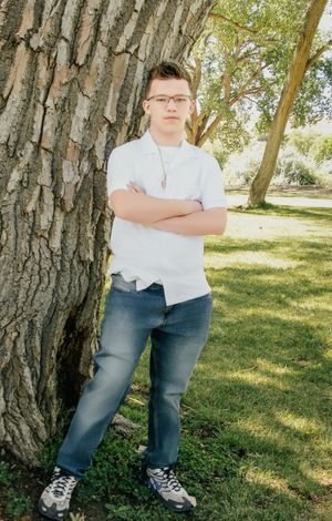 young man posing with arms crossed near a tree with a serious expression