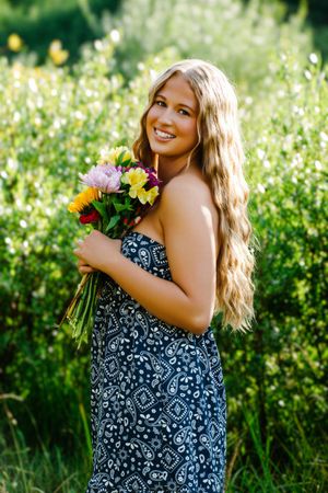 female standing side profile smiling at camera holding flowers