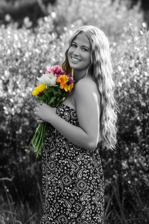 black and white photo of female side profile smiling at camera with color bouquet of flowers
