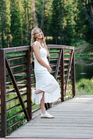 female standing with back up against railing of bridge smiling