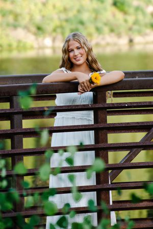 female standing on a bridge smiling holding a sunflower