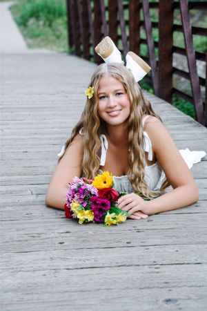 female laying on tummy with legs up crossed holding bouquet of flowers smiling