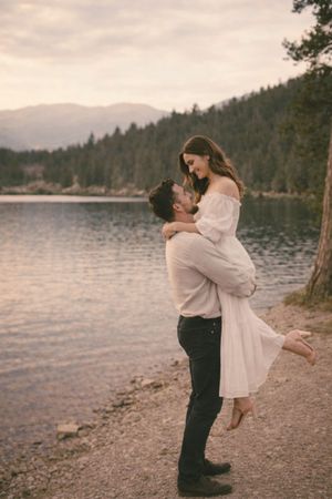 Couple embracing by the lake with mountain backdrop during golden hour photoshoot