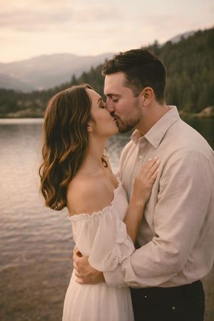Engagement-style portrait of couple sharing a kiss with mountain backdrop