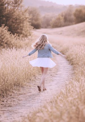 Candid senior photo of young woman spinning on a path at golden hour