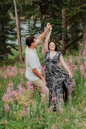 a couple dancing in a field of flowers next to a lake