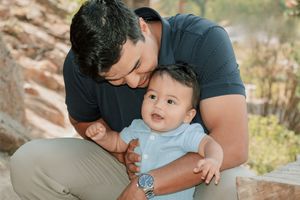 a dad squatted down holding baby from behind both smiling and happy