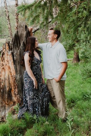 a woman leaning against a tree stump while a man is next to her smiling and talking