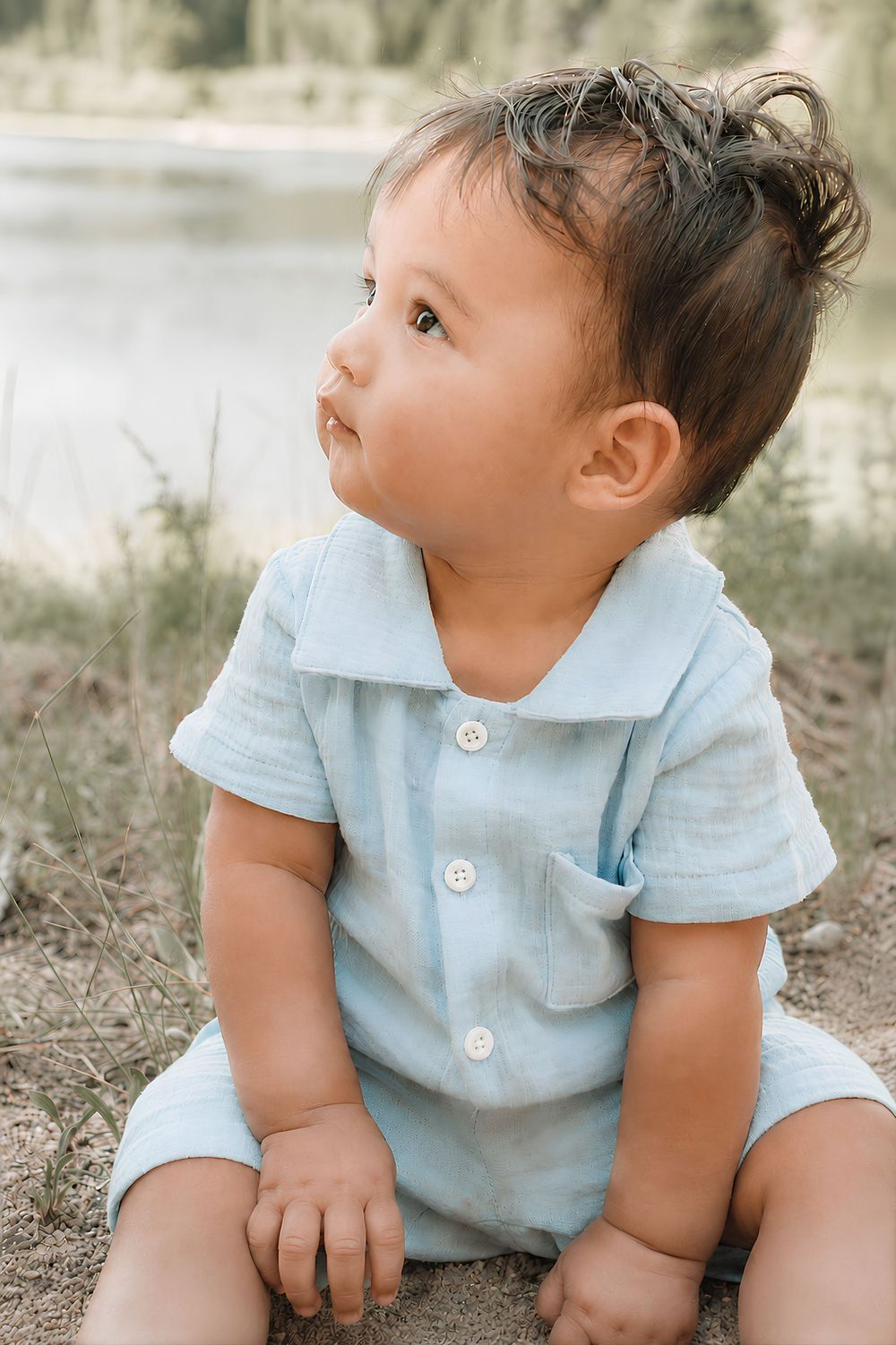 a baby sitting near lake looking up playing in dirt