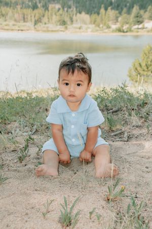 a baby sitting near lake playing in dirt