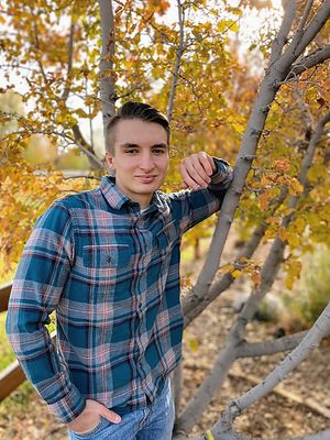 High school senior boy posing by tree with fall foliage during outdoor photoshoot
