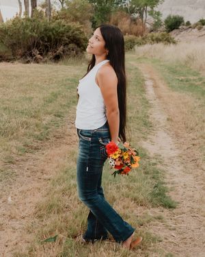 side profile of female standing holding flowers behind back looking off into distance in field
