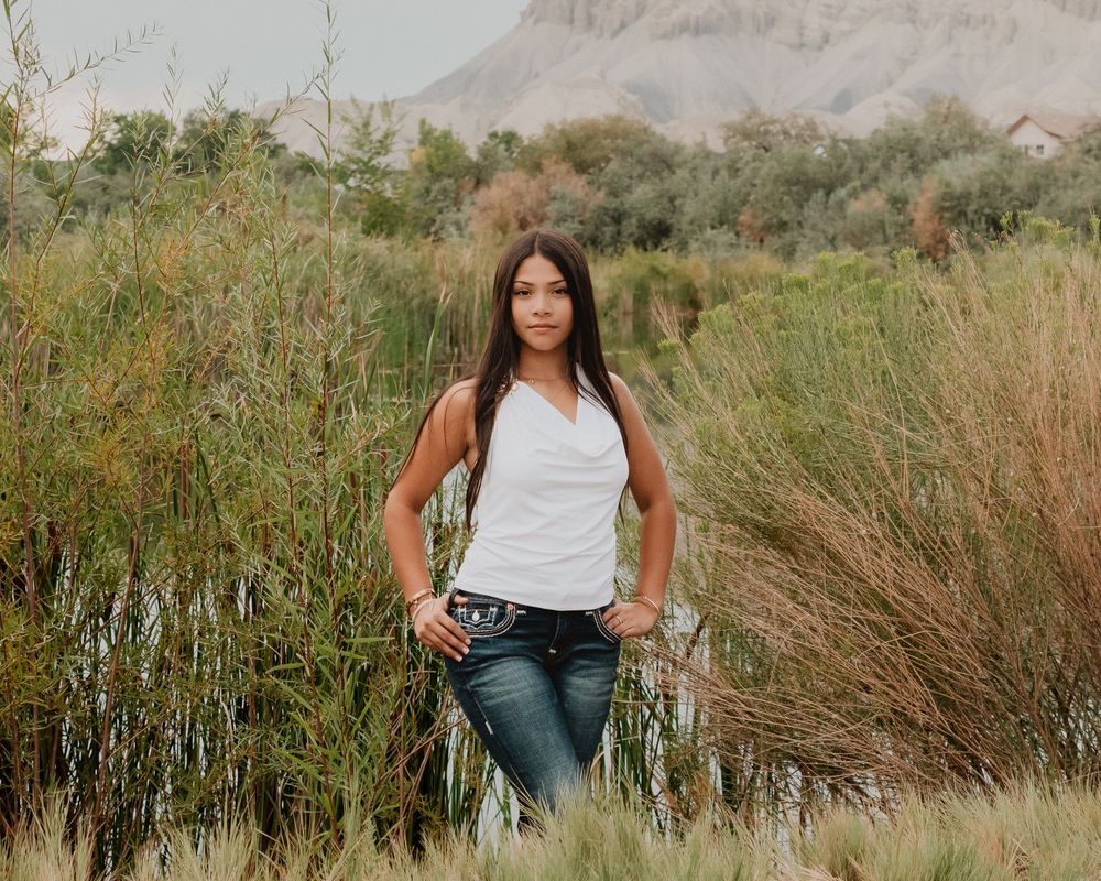 female standing near pond with arms on hips posing
