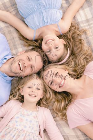 Family lying together on blanket with heads close during outdoor photoshoot