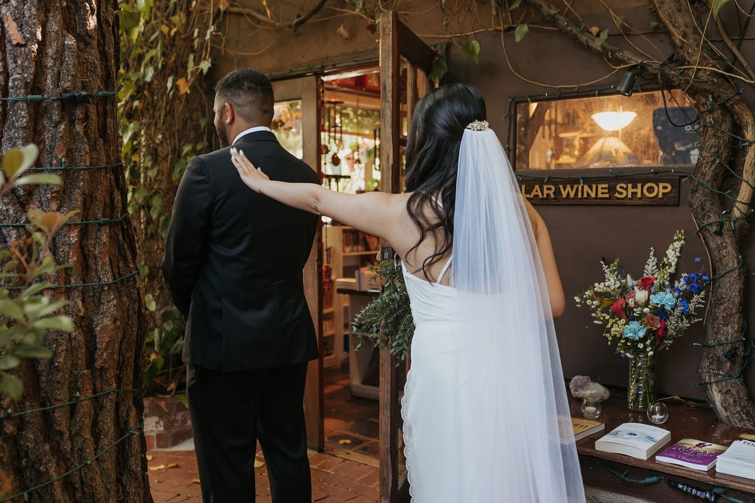 A couple in wedding attire shares an intimate first look moment in a rustic garden setting with string lights overhead.