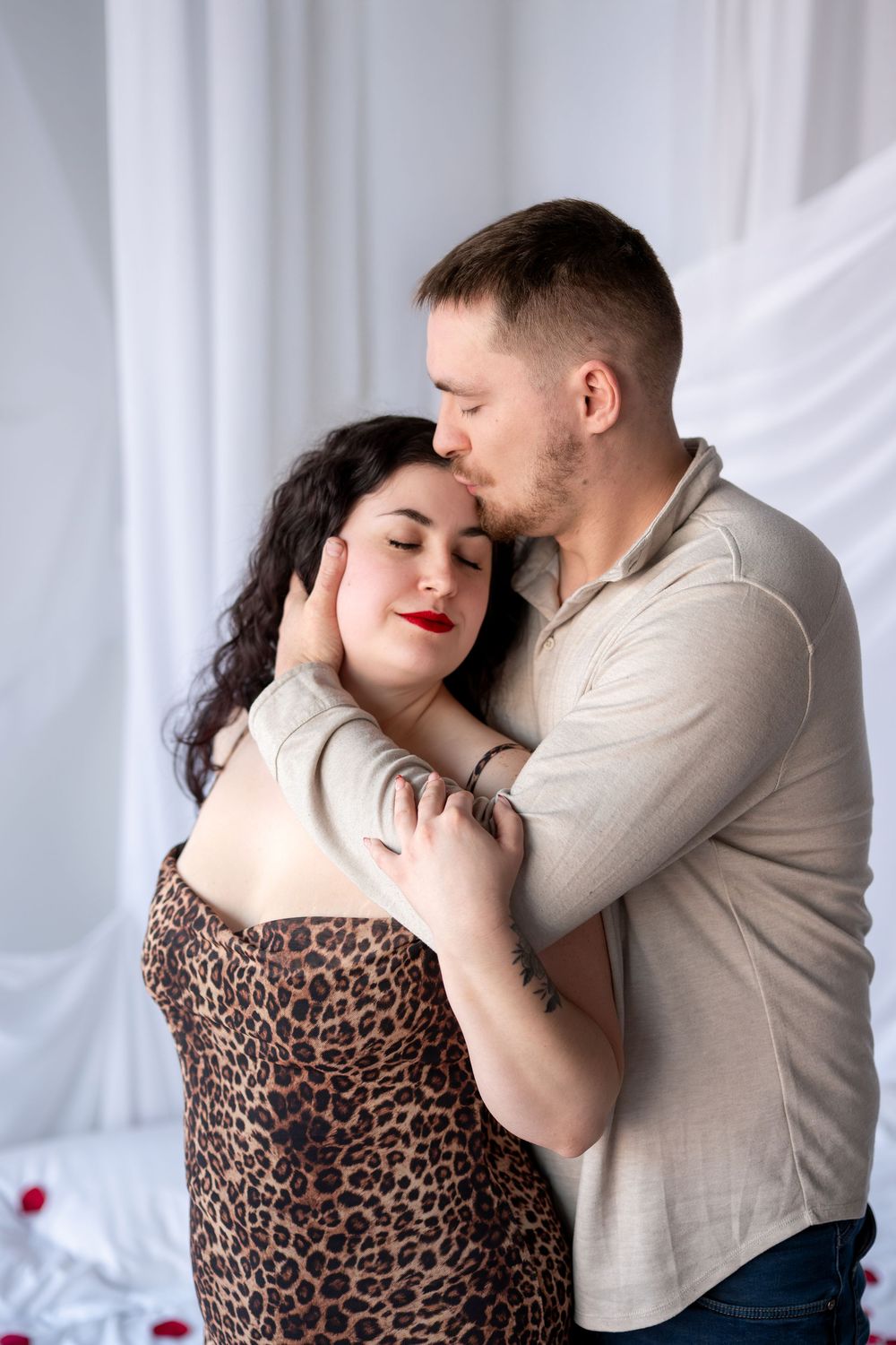 Man gently kisses woman with red lips in leopard dress while holding her face tenderly.