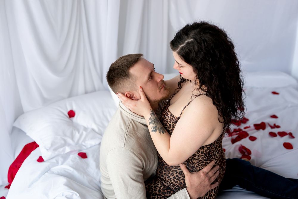 Couple sharing a tender moment together on a white bed surrounded by romantic red rose petals.