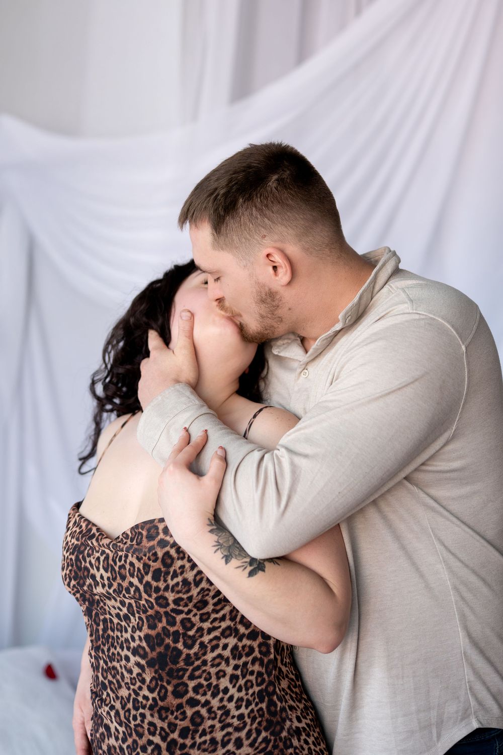 Romantic couple sharing a passionate kiss, man embracing woman in leopard print dress indoors.