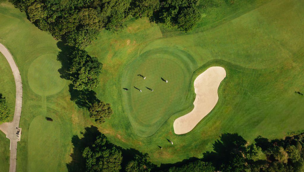 Aerial view of a lush green golf course with sand bunkers and winding cart paths stretching across the landscape.
