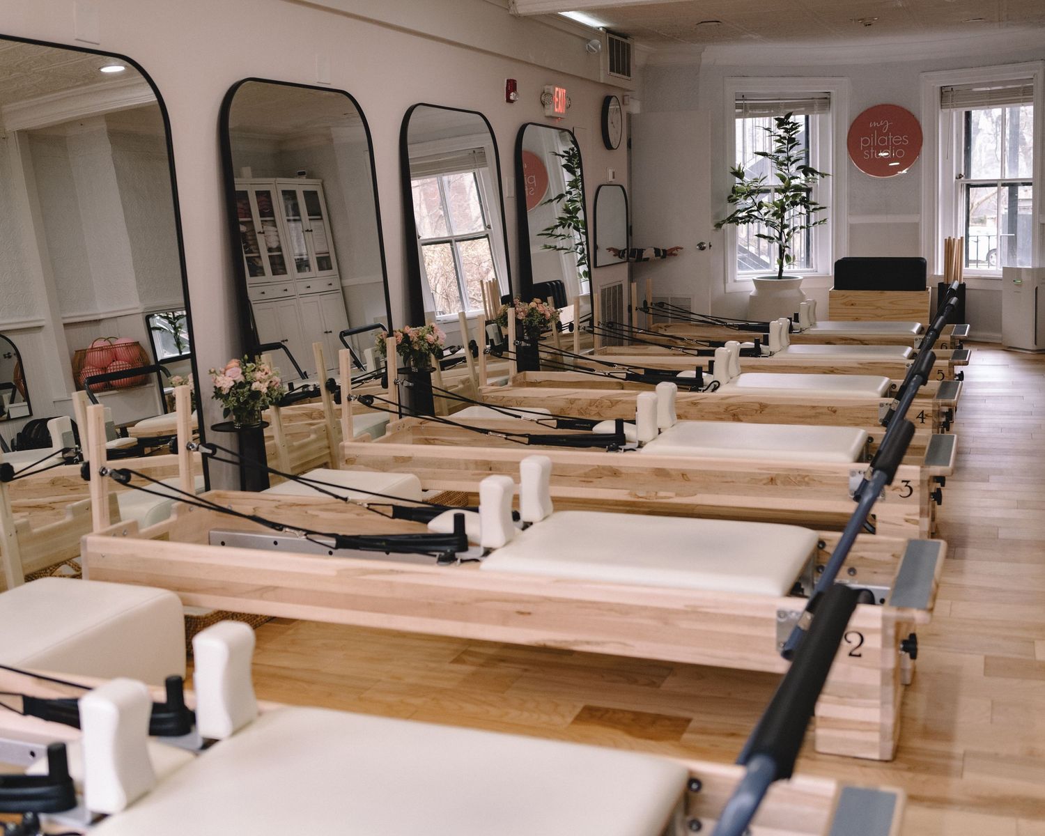 Modern pilates studio interior with multiple reformer machines and natural light streaming through large windows.