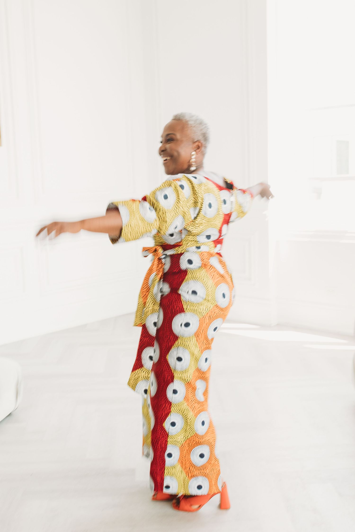 Person wearing vibrant floral kimono-style robe with orange and yellow pattern strikes dynamic poses in white studio space.