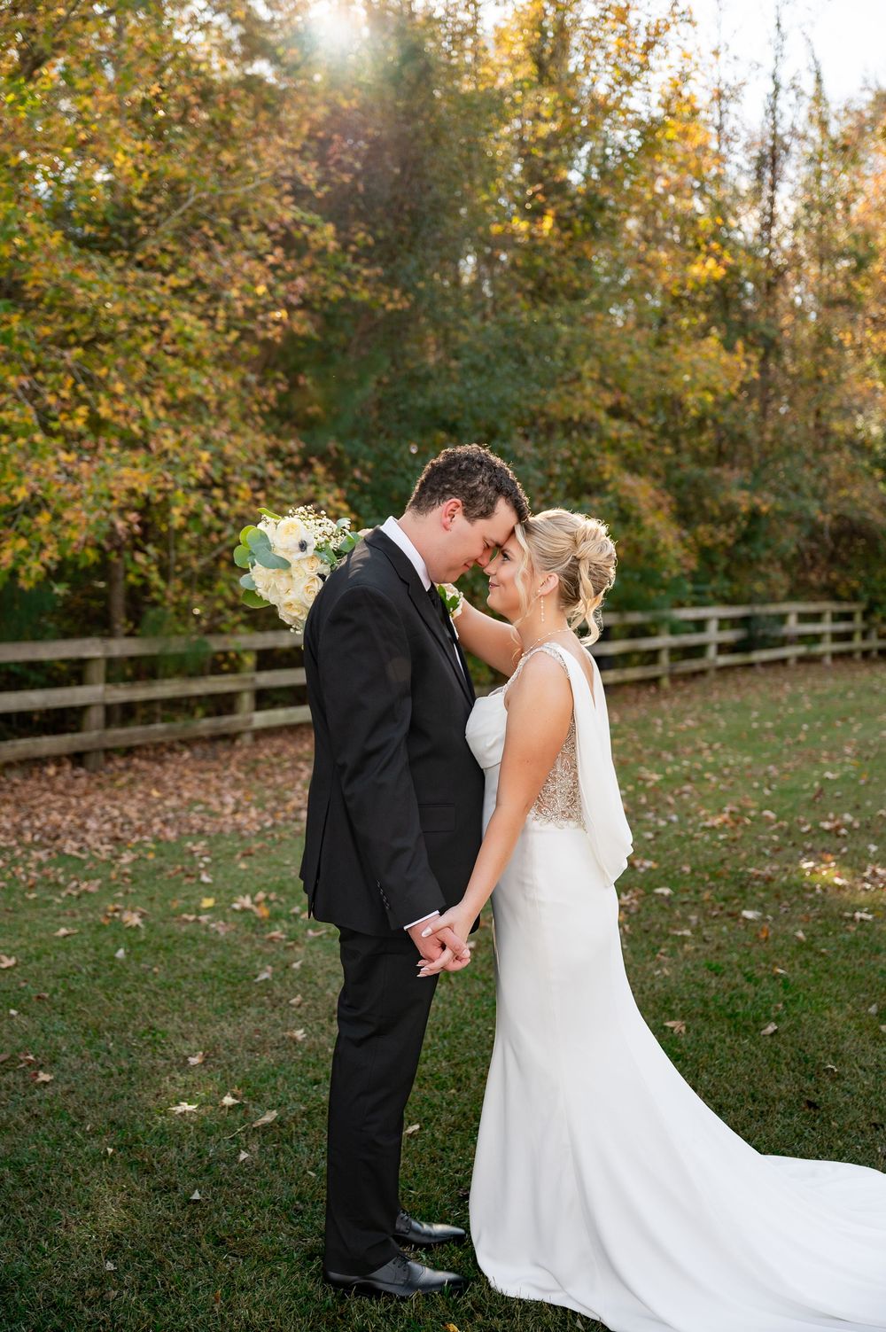 Romantic wedding couple shares intimate moment in autumn garden with wooden fence backdrop.