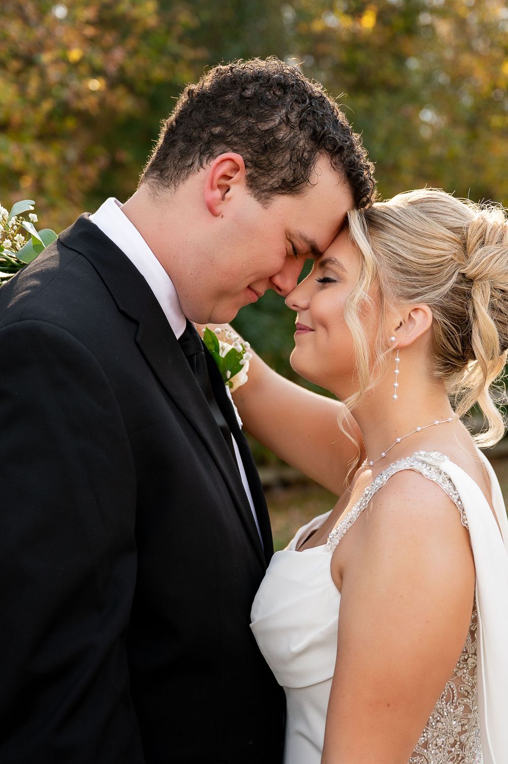 Romantic close-up wedding portrait with couple touching foreheads outdoors.