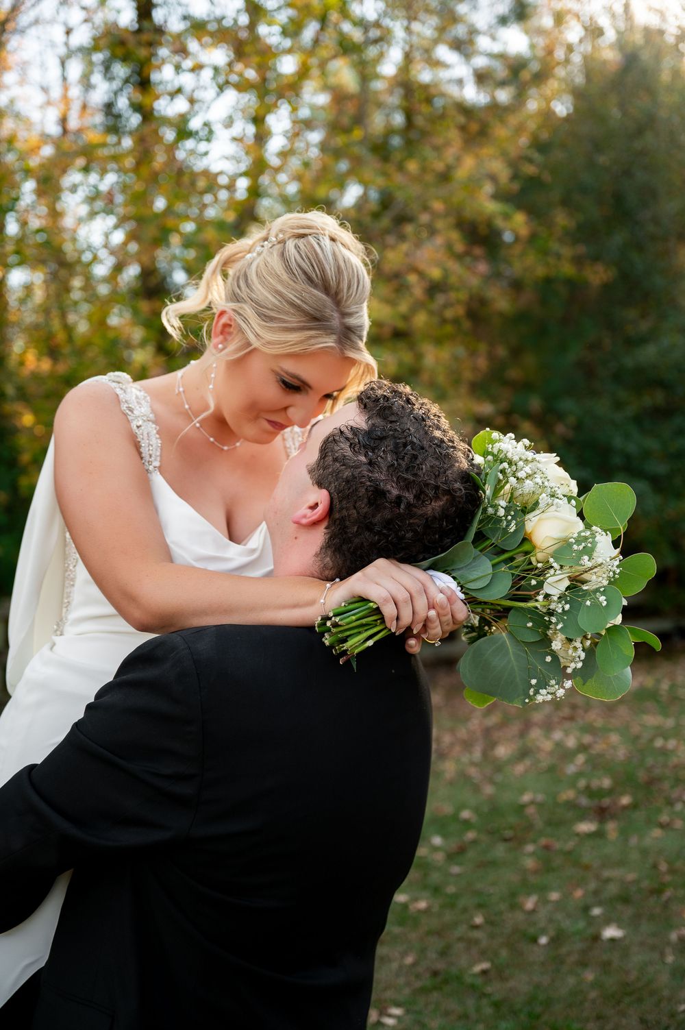 Romantic dip pose with white bouquet during outdoor autumn wedding photoshoot.
