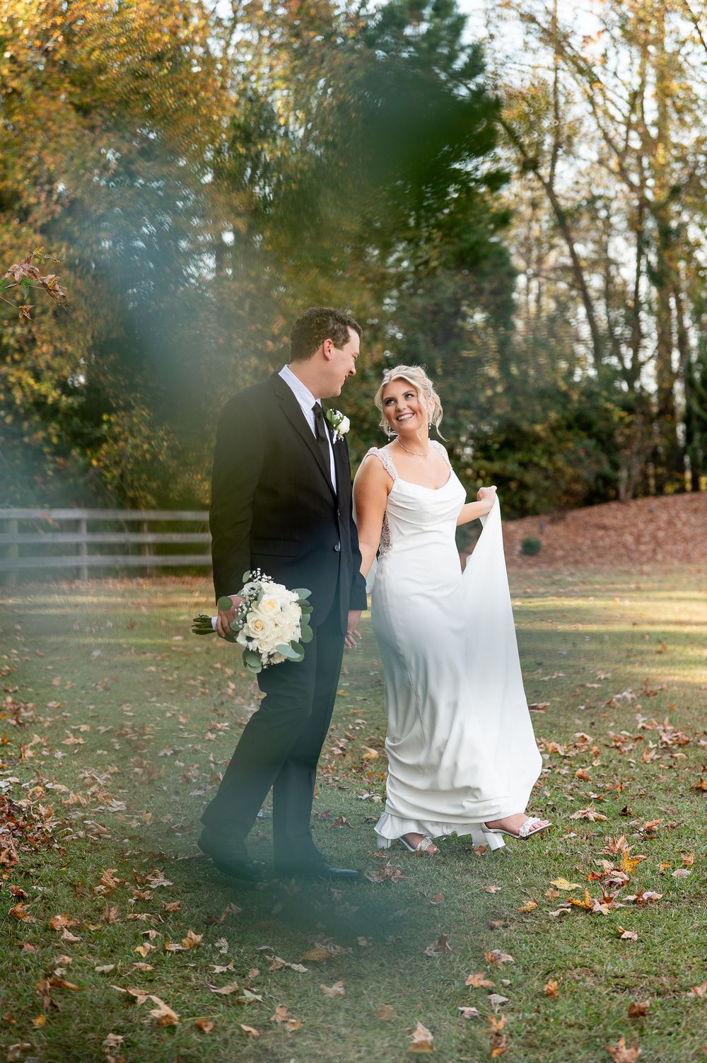 Newlyweds share romantic moment on lawn with sunlit autumn trees.