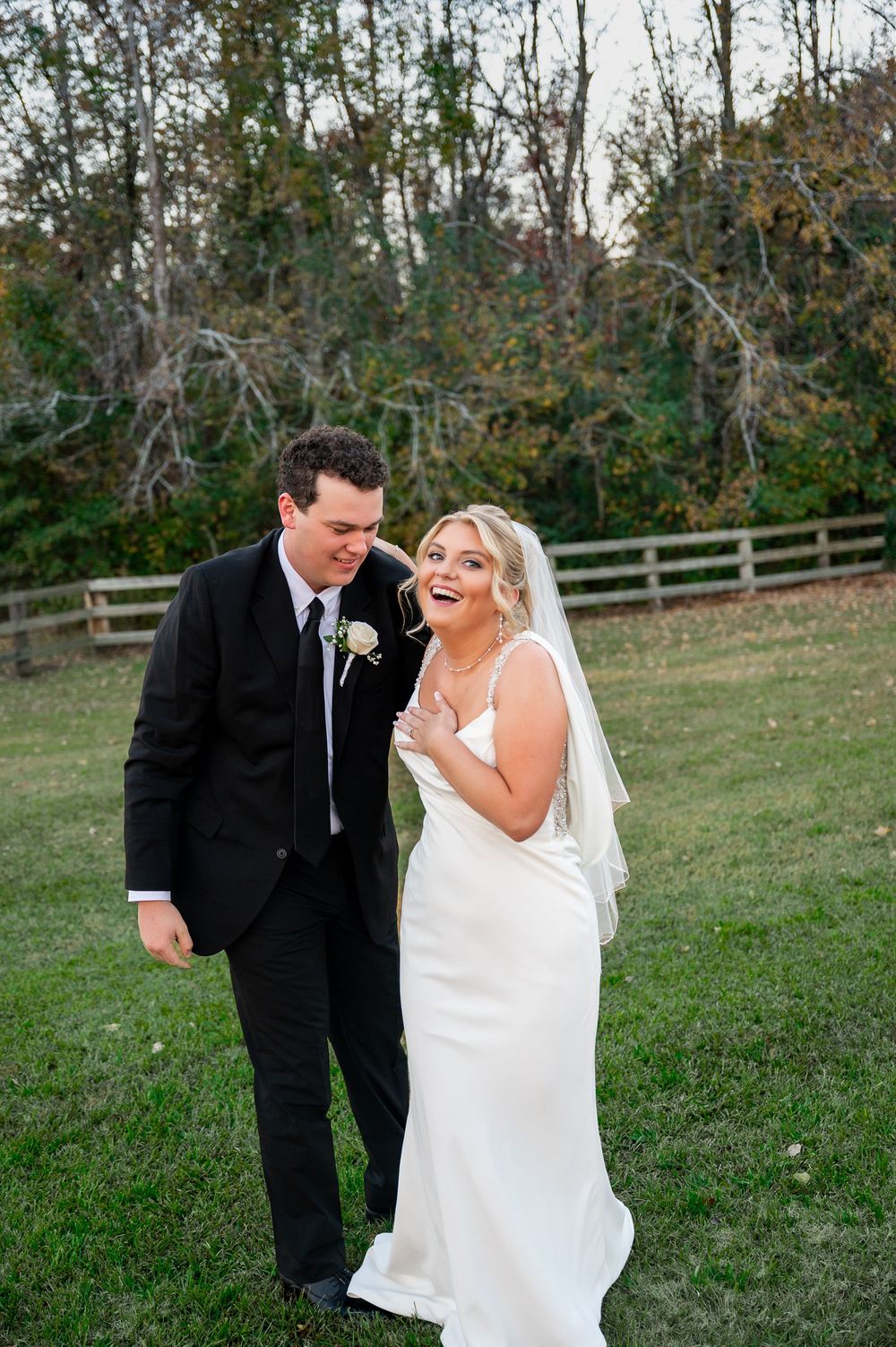 Candid wedding moment with couple laughing together on grassy lawn.