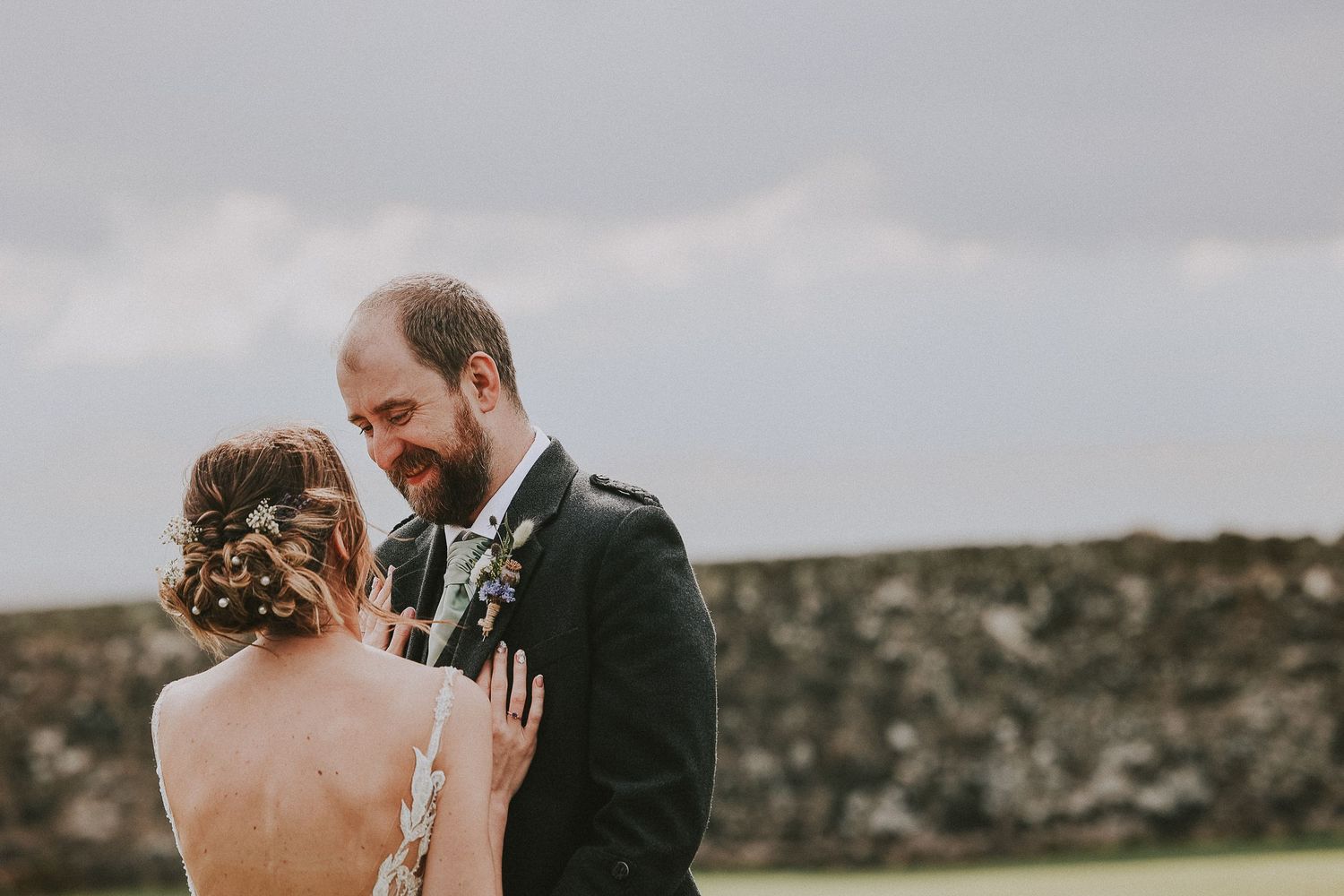 Romantic wedding couple embracing against cloudy mountain backdrop.