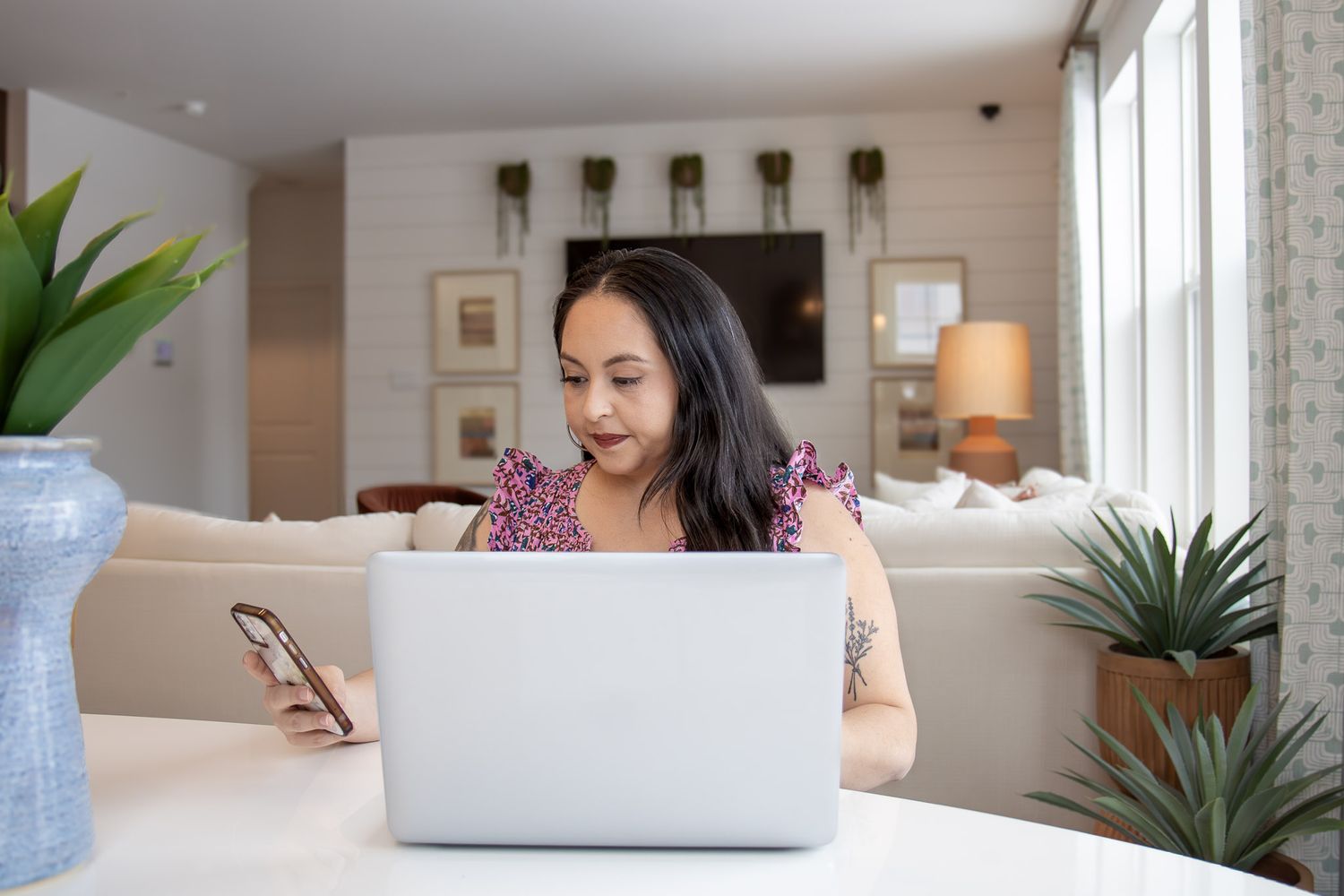 Person working from home on laptop in bright modern living room with houseplants and natural light.
