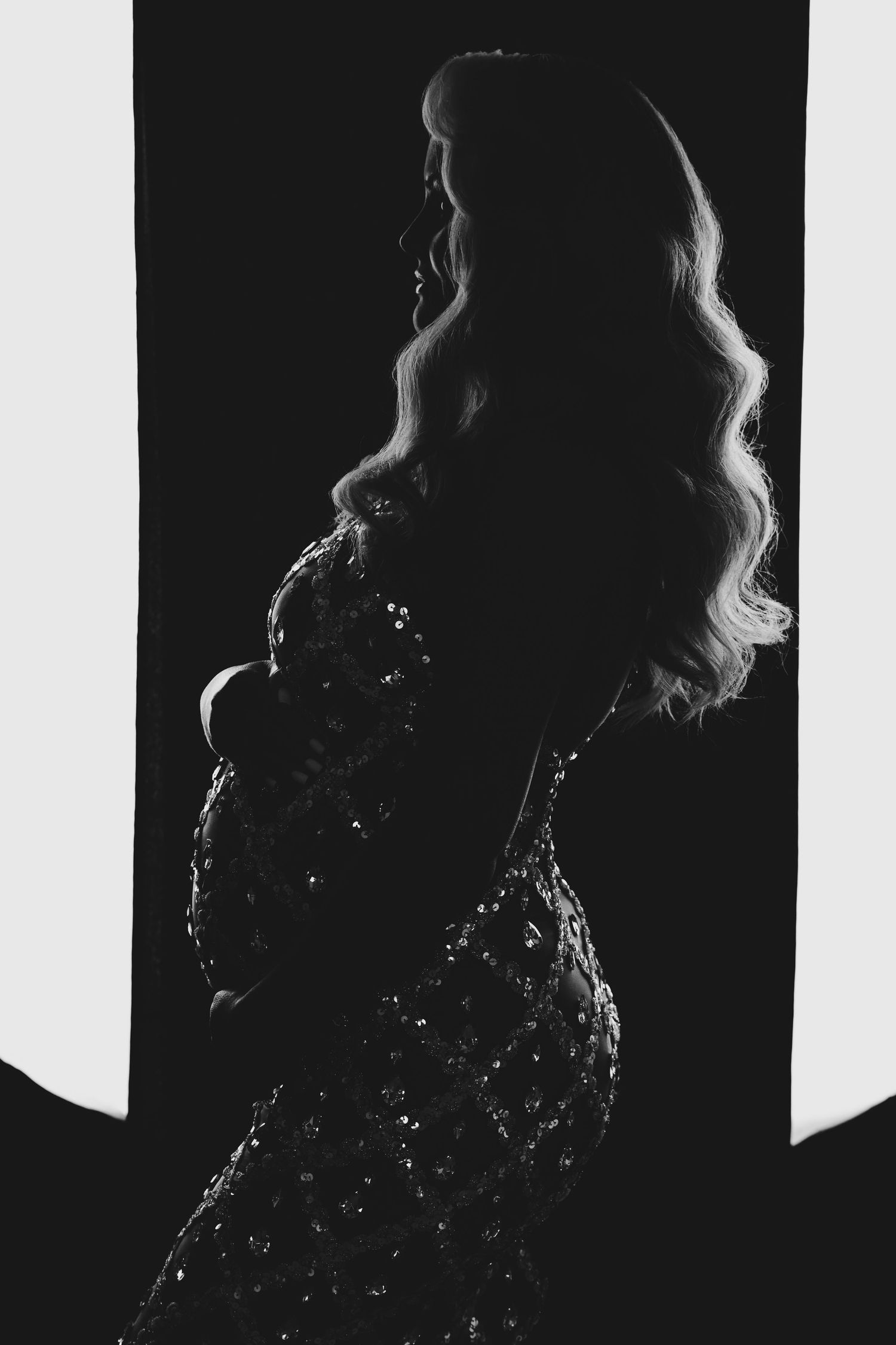 Silhouetted figure in a sparkling dress stands in dramatic lighting with long wavy hair against dark background.
