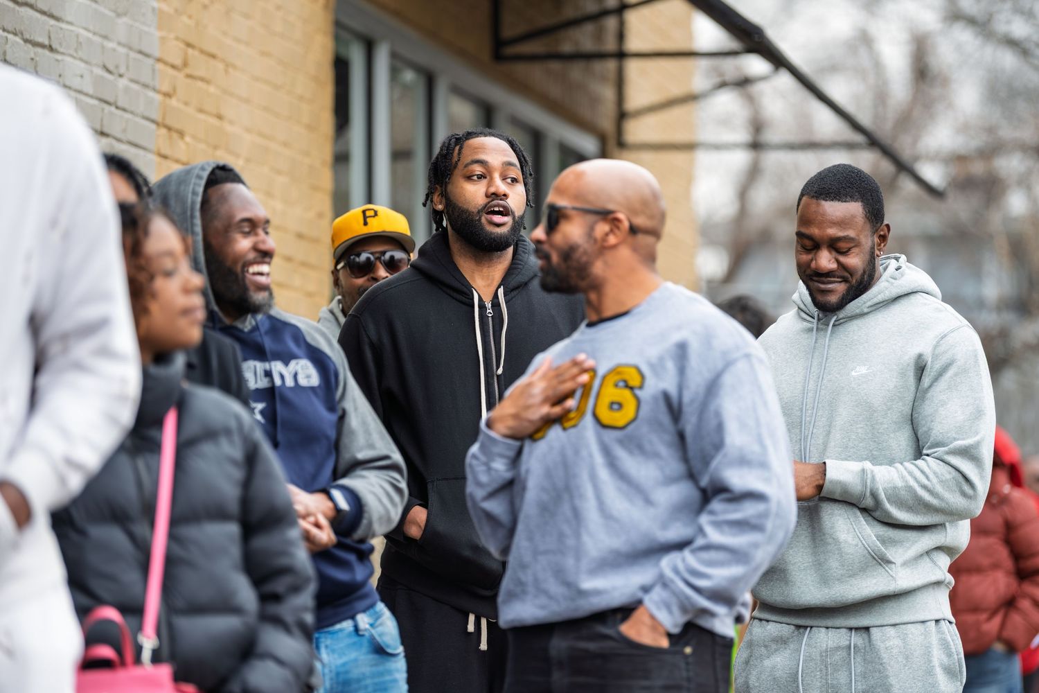 A group of people stand outside in casual clothing having a conversation on a sunny day.