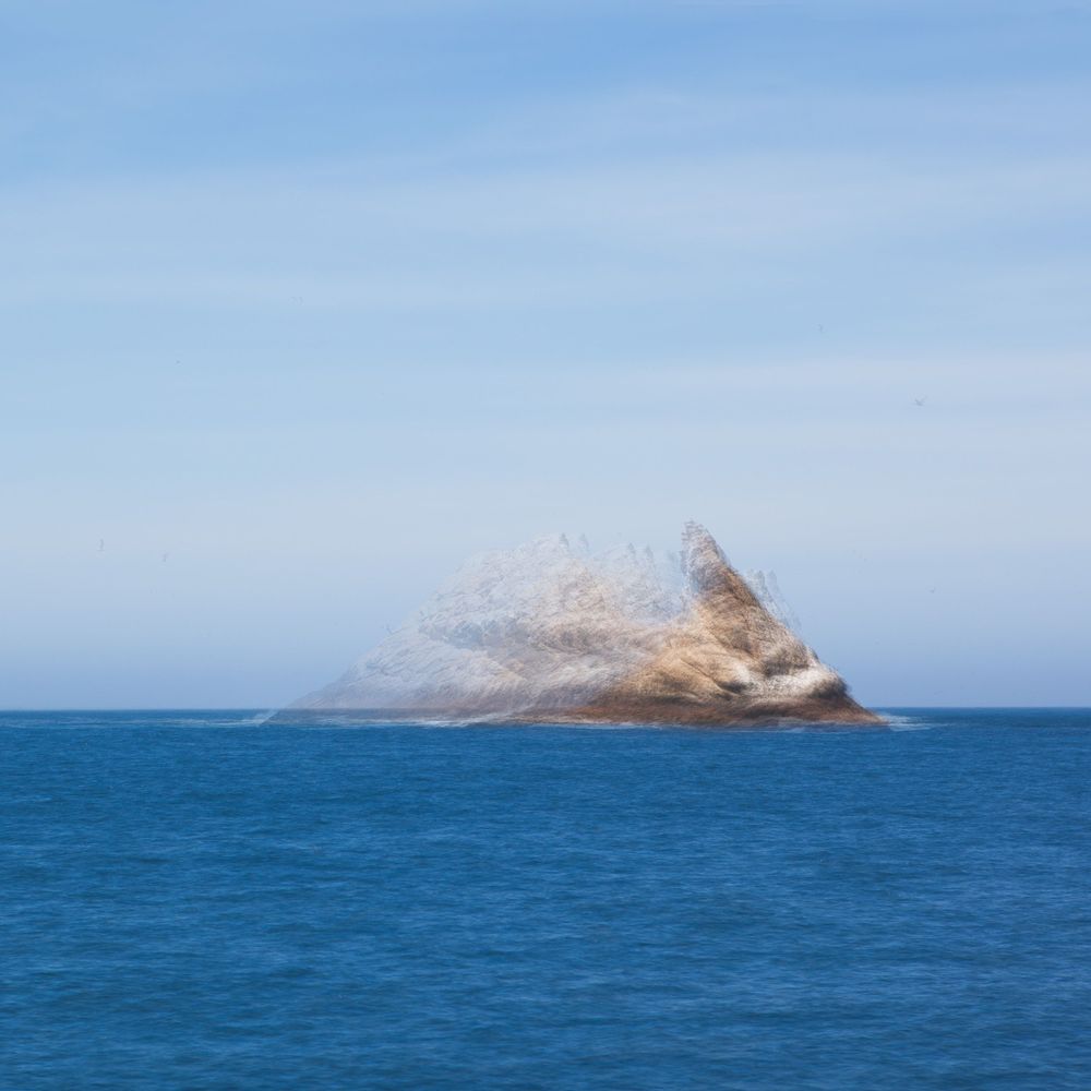 Rocky island formation emerging from bright blue ocean waters.